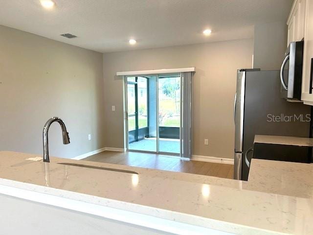 kitchen featuring light stone countertops, white cabinets, light hardwood / wood-style floors, and kitchen peninsula