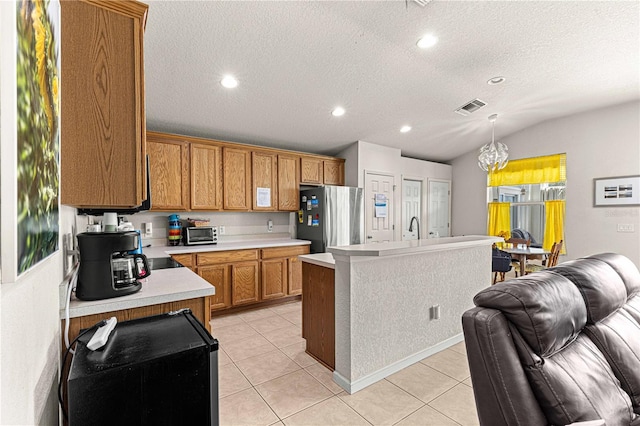 kitchen with stainless steel fridge, pendant lighting, lofted ceiling, a center island with sink, and a notable chandelier