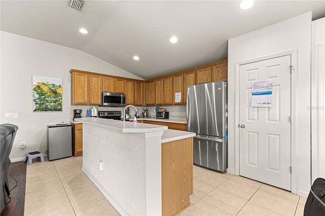 kitchen featuring a kitchen island with sink, appliances with stainless steel finishes, lofted ceiling, and light tile patterned flooring