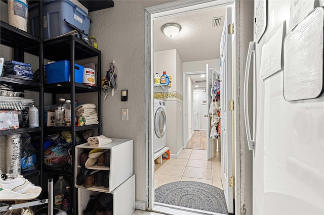 laundry area featuring a textured ceiling, light tile patterned floors, and washing machine and dryer