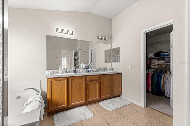 bathroom with a bathing tub, vaulted ceiling, vanity, and tile patterned floors