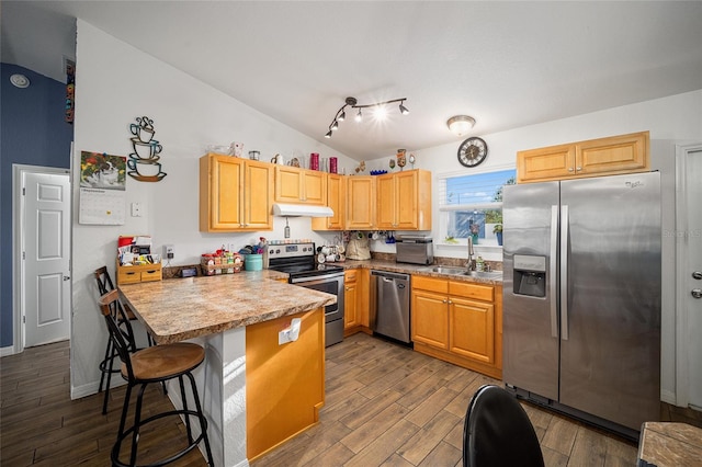 kitchen featuring sink, vaulted ceiling, a kitchen breakfast bar, stainless steel appliances, and hardwood / wood-style floors