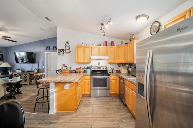 kitchen featuring ceiling fan, lofted ceiling, a kitchen bar, appliances with stainless steel finishes, and light hardwood / wood-style floors