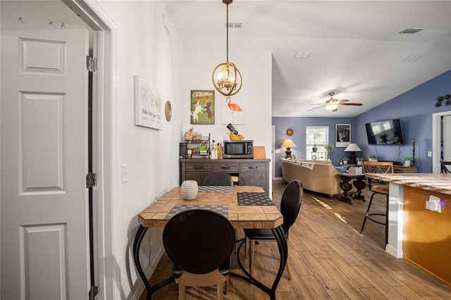 dining space featuring ceiling fan with notable chandelier, light wood-type flooring, and lofted ceiling