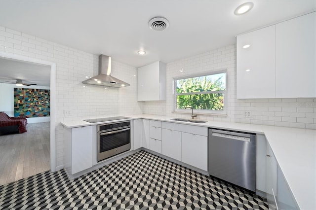 kitchen with stainless steel appliances, a sink, visible vents, light countertops, and wall chimney exhaust hood