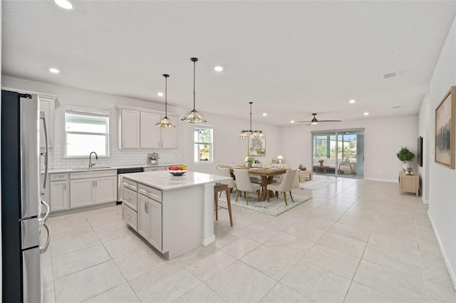 kitchen featuring backsplash, stainless steel appliances, ceiling fan, pendant lighting, and a kitchen island