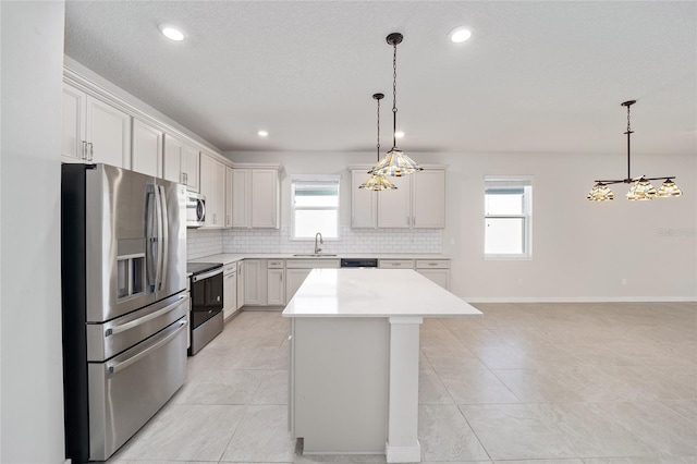 kitchen featuring appliances with stainless steel finishes, an inviting chandelier, white cabinets, a center island, and hanging light fixtures