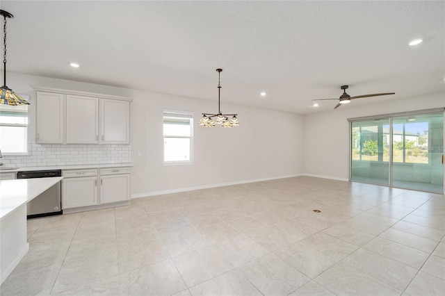 kitchen with backsplash, white cabinets, ceiling fan with notable chandelier, stainless steel dishwasher, and decorative light fixtures