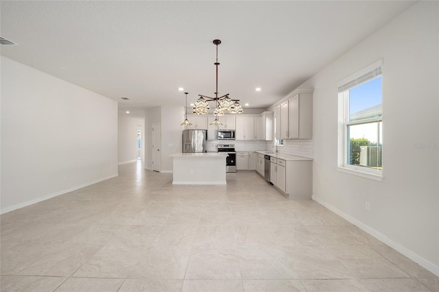 kitchen with tasteful backsplash, a notable chandelier, decorative light fixtures, a kitchen island, and appliances with stainless steel finishes