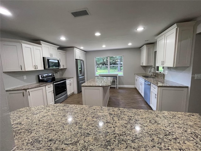 kitchen with light stone countertops, appliances with stainless steel finishes, sink, white cabinets, and a center island