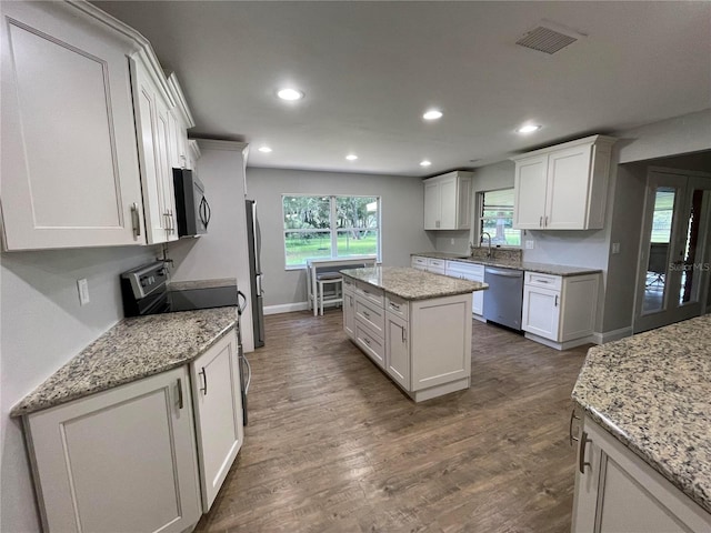 kitchen featuring appliances with stainless steel finishes, dark hardwood / wood-style flooring, light stone counters, white cabinets, and a center island