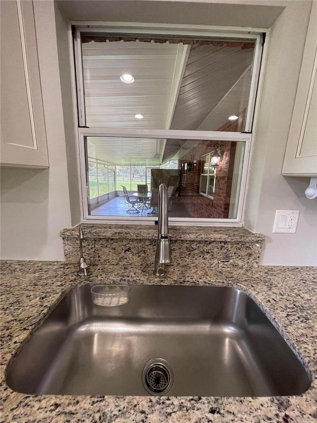 details with white cabinetry, light stone counters, and sink