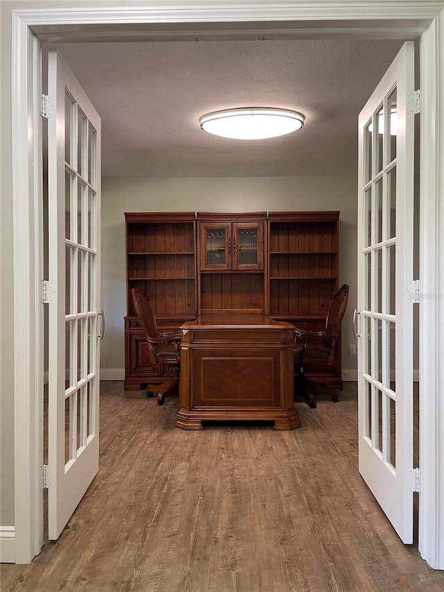 office with french doors, a textured ceiling, hardwood / wood-style flooring, and built in desk