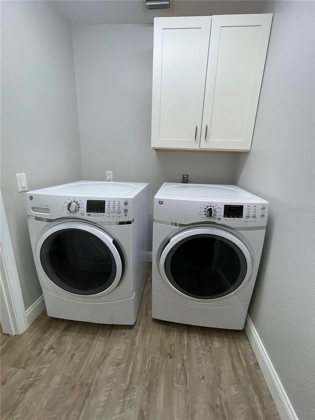 laundry room with washing machine and dryer, light wood-type flooring, and cabinets