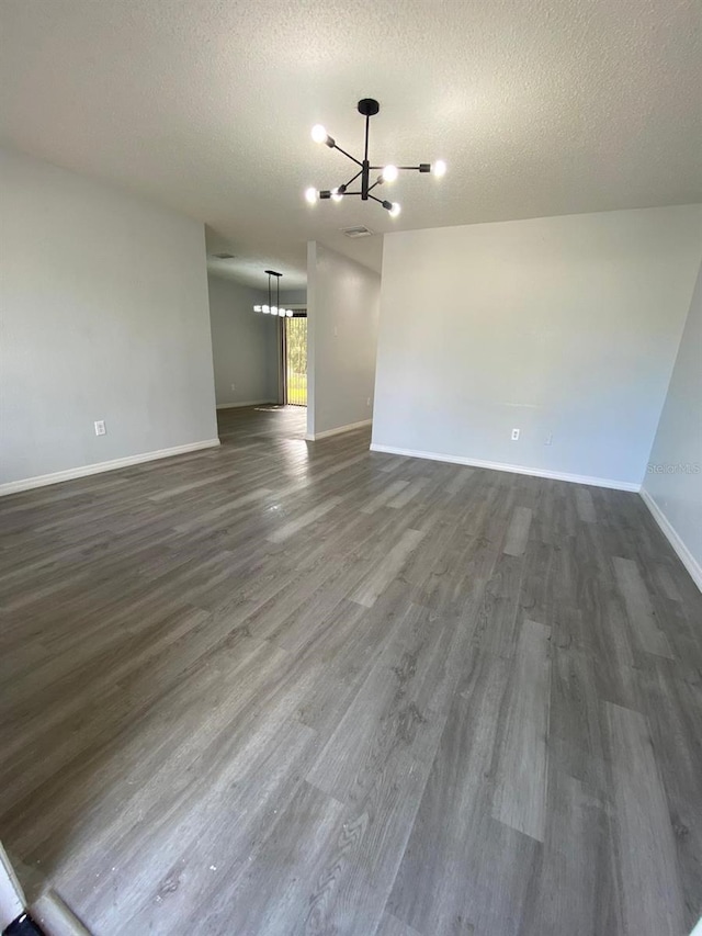 unfurnished living room featuring a chandelier, a textured ceiling, and dark hardwood / wood-style flooring