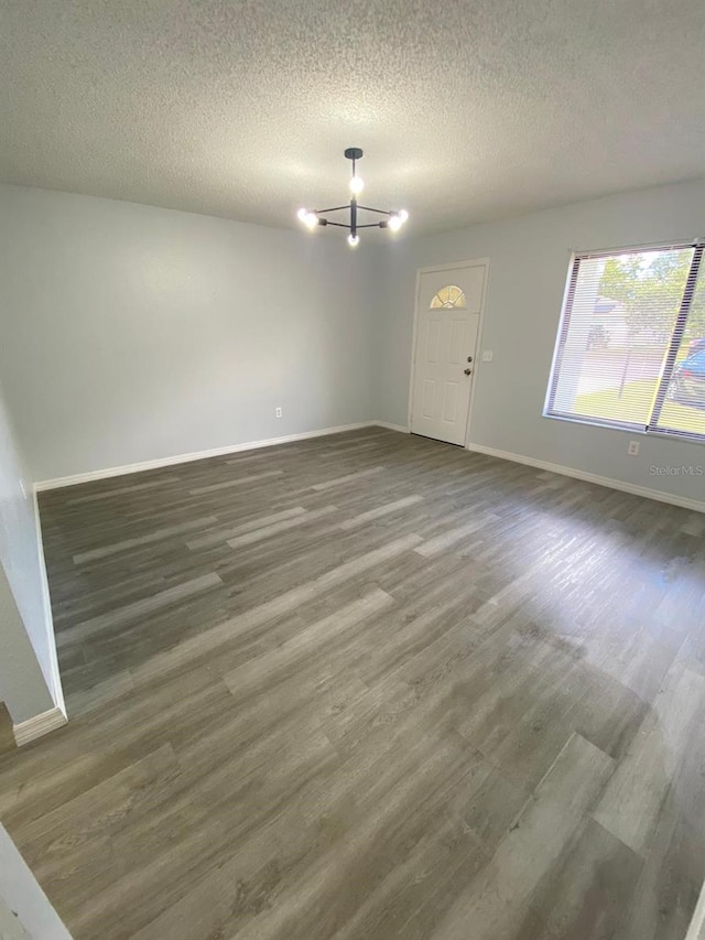 unfurnished room with a textured ceiling, a chandelier, and dark hardwood / wood-style flooring