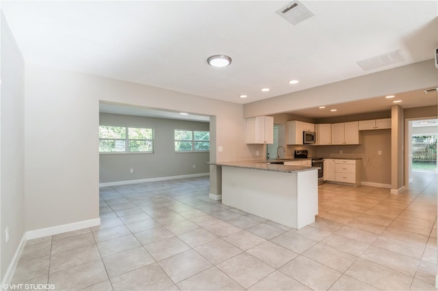 kitchen featuring white cabinetry, stainless steel appliances, light stone counters, and a wealth of natural light