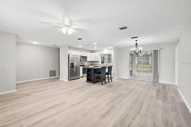 unfurnished living room with a textured ceiling, ceiling fan with notable chandelier, and light hardwood / wood-style floors