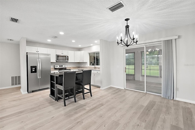 kitchen featuring pendant lighting, light wood-type flooring, a center island, white cabinets, and stainless steel appliances