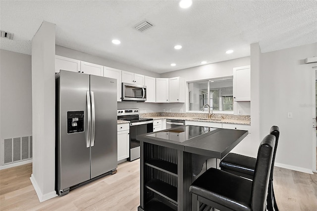 kitchen with light hardwood / wood-style floors, appliances with stainless steel finishes, sink, and white cabinetry