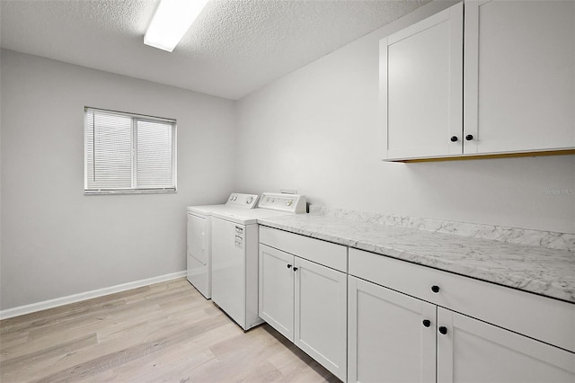 washroom with a textured ceiling, washing machine and dryer, light hardwood / wood-style flooring, and cabinets