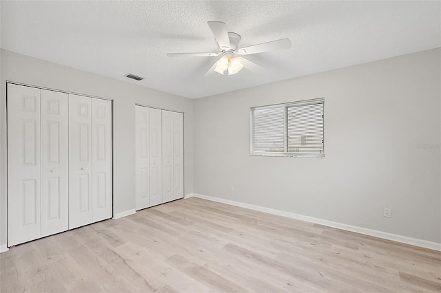 unfurnished bedroom with ceiling fan, multiple closets, a textured ceiling, and light hardwood / wood-style floors