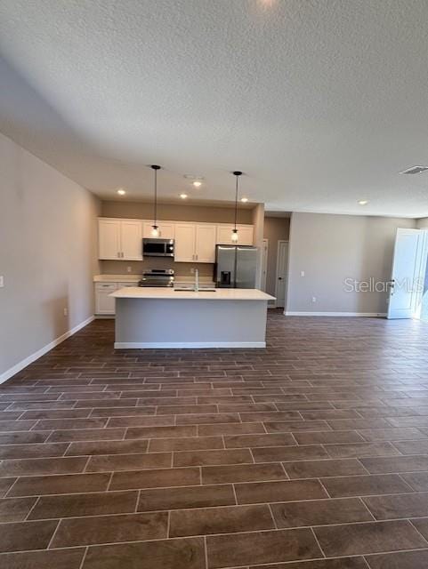 kitchen featuring sink, hanging light fixtures, stainless steel appliances, an island with sink, and white cabinets