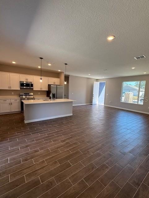 kitchen featuring sink, appliances with stainless steel finishes, white cabinetry, a kitchen island with sink, and decorative light fixtures