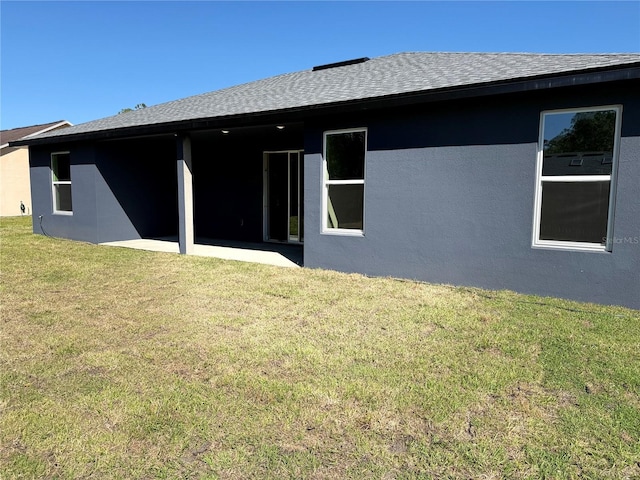 rear view of property with a yard, stucco siding, and roof with shingles