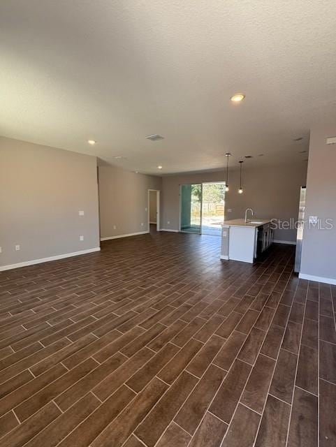unfurnished living room featuring a sink, dark wood-type flooring, and baseboards