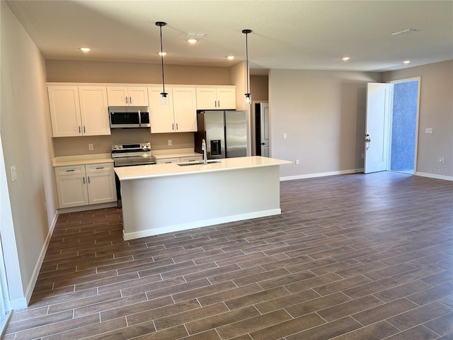 kitchen with baseboards, a kitchen island with sink, appliances with stainless steel finishes, a sink, and dark wood-style floors