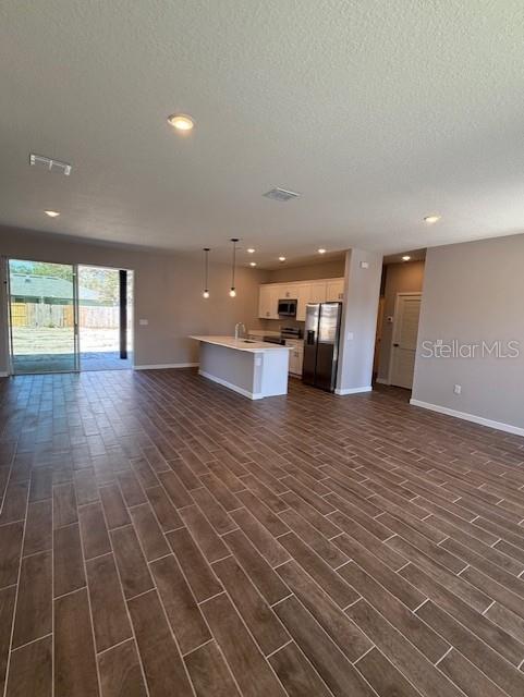 unfurnished living room with a textured ceiling, visible vents, dark wood-style floors, baseboards, and recessed lighting