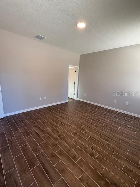 spare room with a textured ceiling, visible vents, baseboards, wood finish floors, and recessed lighting