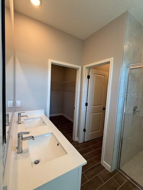 bathroom with double vanity, a walk in closet, a stall shower, and a sink