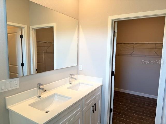 bathroom with double vanity, wood finished floors, a spacious closet, and a sink