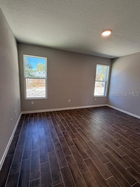 spare room featuring baseboards, a textured ceiling, and dark wood-type flooring