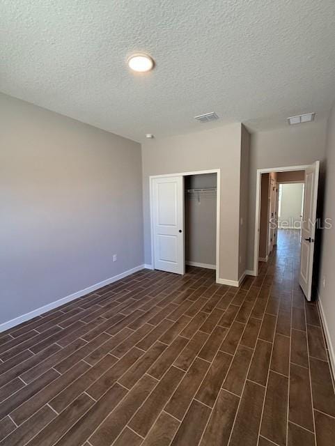 unfurnished bedroom with baseboards, a textured ceiling, dark wood-style flooring, and a closet