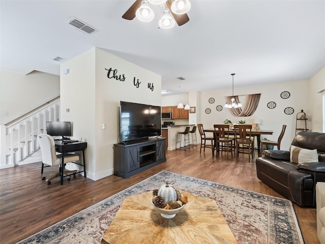 living room with dark hardwood / wood-style flooring and ceiling fan with notable chandelier