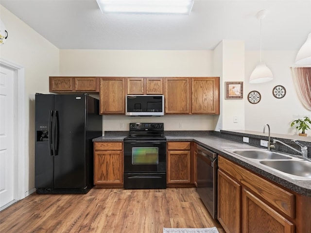 kitchen featuring sink, kitchen peninsula, decorative light fixtures, black appliances, and light wood-type flooring