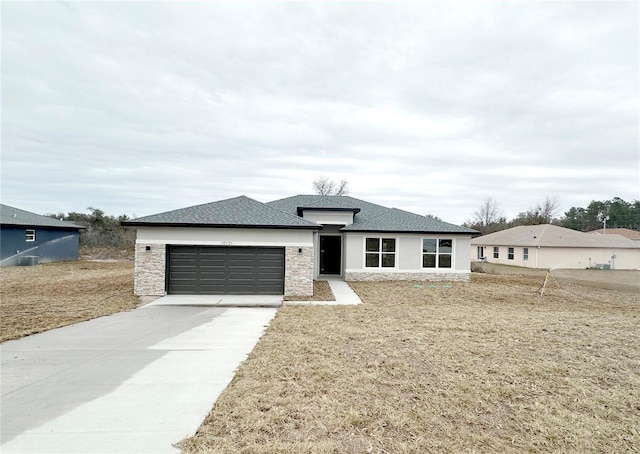 prairie-style home featuring an attached garage, a shingled roof, a front lawn, and concrete driveway