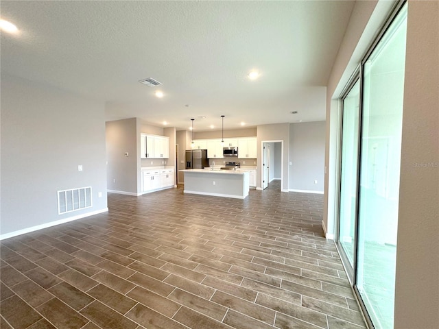 unfurnished living room with a textured ceiling, dark wood finished floors, visible vents, and baseboards