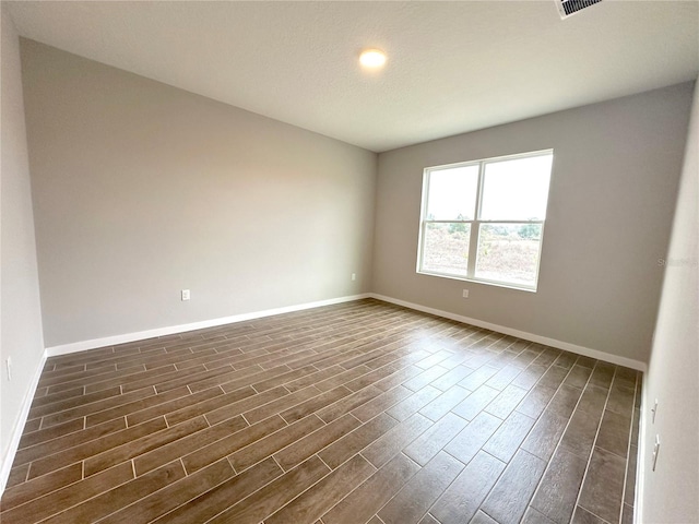 spare room featuring dark wood-type flooring, visible vents, and baseboards