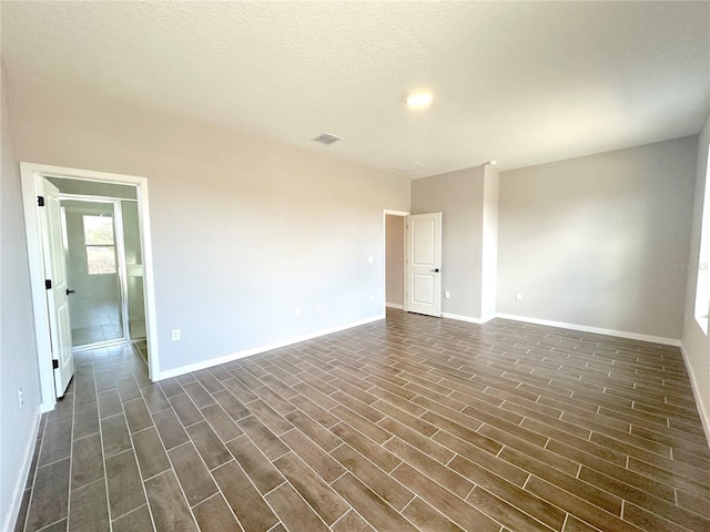 empty room featuring dark wood-style floors, a textured ceiling, visible vents, and baseboards