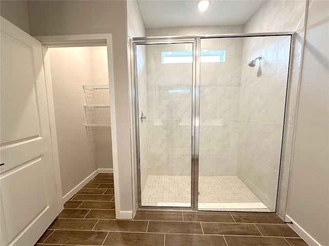 full bath with a spacious closet, wood finish floors, a stall shower, and baseboards