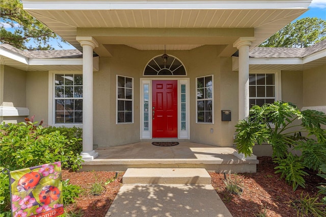 view of exterior entry featuring a porch, stucco siding, and a shingled roof