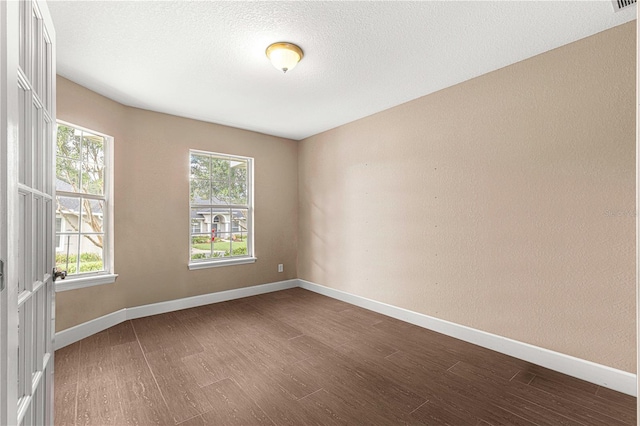 spare room with a textured ceiling, dark wood-style flooring, and baseboards