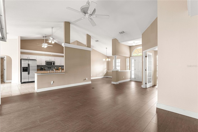 unfurnished living room with high vaulted ceiling, decorative columns, a notable chandelier, and hardwood / wood-style floors