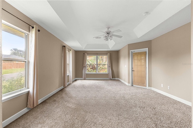 empty room featuring light carpet, a tray ceiling, baseboards, and ceiling fan