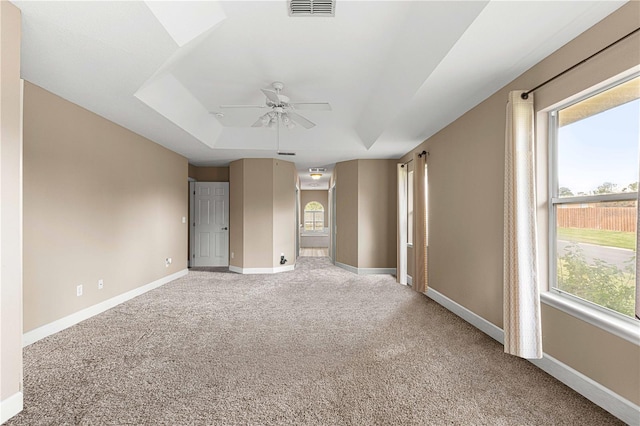 empty room with visible vents, baseboards, ceiling fan, a tray ceiling, and light colored carpet