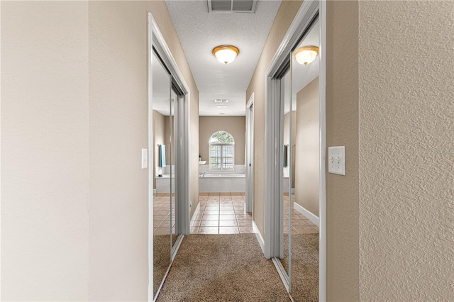 hall with a textured wall, tile patterned flooring, a textured ceiling, visible vents, and carpet